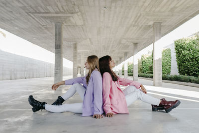 Young sisters sitting back to back on floor at parking lot