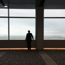 Rear view of silhouette man looking through window