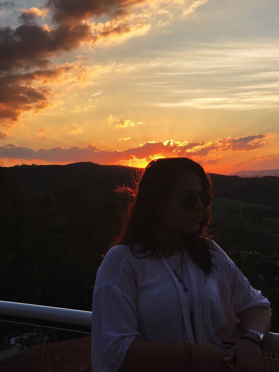 sunset, sky, real people, cloud - sky, orange color, one person, beauty in nature, lifestyles, leisure activity, nature, scenics - nature, railing, standing, non-urban scene, young adult, front view, looking, waist up, young women, hairstyle, outdoors, looking at view, teenager