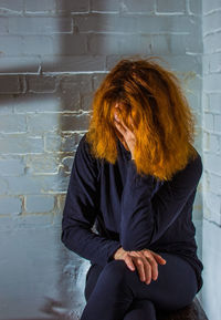 Tensed woman sitting against brick wall