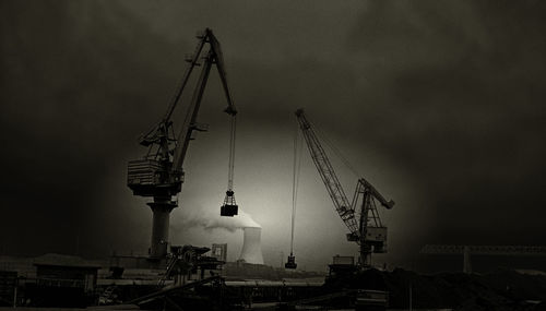 Cranes in city against sky at night
