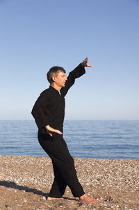 Man with arms raised on beach against clear sky