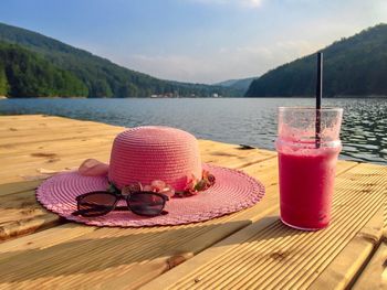 Pink summer hat, sunglasses and pink smoothie in a glass on wooden pontoon near the lake