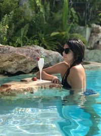 Side view of mid adult woman wearing sunglasses swimming in pool