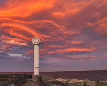 Lighthouse by sea against sky during sunset