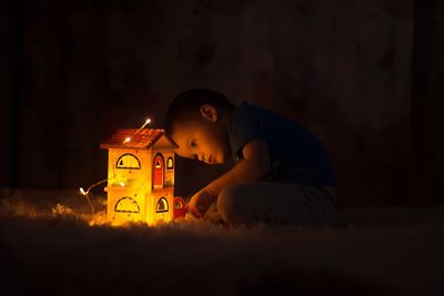 Boy playing with illuminated model home in darkroom