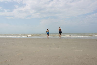 Rear view of people standing at beach against sky