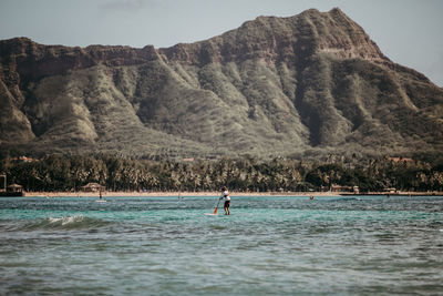 Man on stand up paddle in sea against mountains