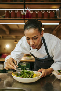 Female chef garnishing salad with cilantro using tweezers in commercial kitchen