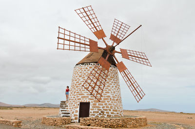 Woman standing on traditional windmill against sky