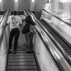 Rear view of people standing on escalator at railroad station