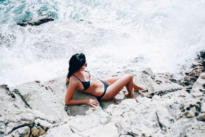 Woman in bikini sitting on rock at beach