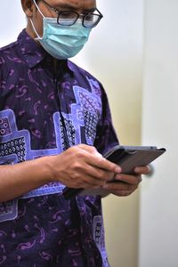 Midsection of man holding mobile phone while standing against wall