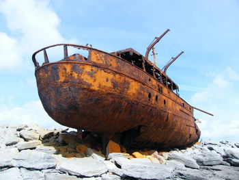 Shipwreck at rocky shore against sky