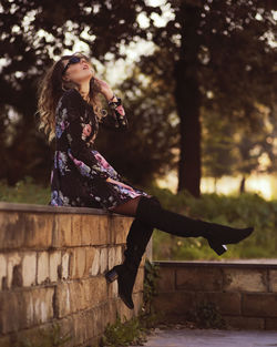 Woman looking away while sitting on tree against plants