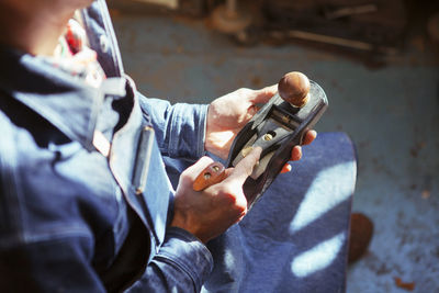 Midsection of carpenter holding wood plane at workshop