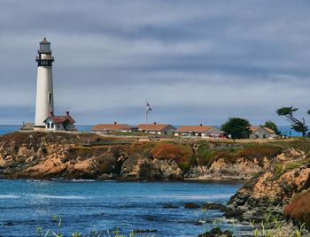 View of lighthouse by sea against buildings