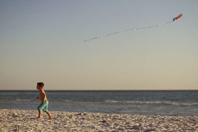 Boy running on sand at beach against sky