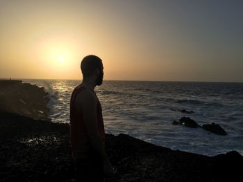 Silhouette man standing on beach against sky during sunset