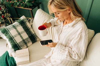 Young woman employee browsing data on smartphone and analyzing stock charts while drinking coffee.