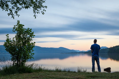 Rear view of man standing on lakeshore against sky