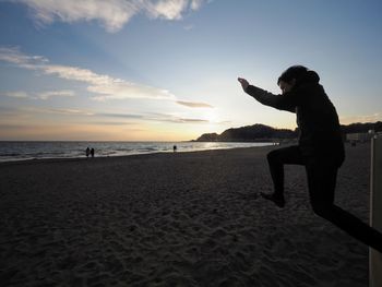 Silhouette man jumping at beach against sky during sunset