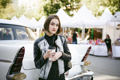 Portrait of beautiful woman having coffee by car on road