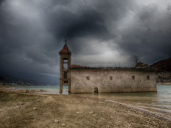 Tower on beach against cloudy sky