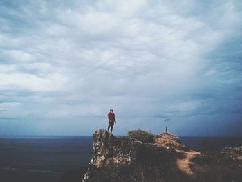 Man standing on rock by sea against sky