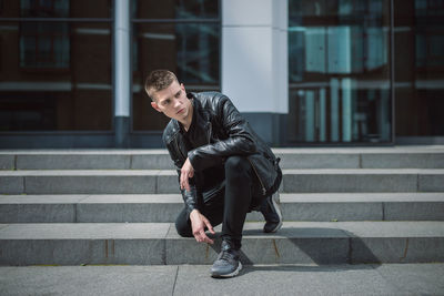 Thoughtful young man sitting kneeling on steps against building