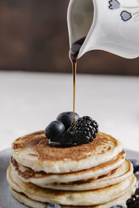 A jar pouring syrup on top of a stack of homemade pancakes with