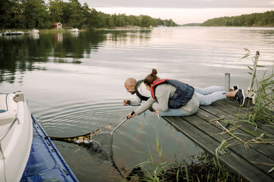 Smiling father helping daughter remove slipper from lake through fishing net