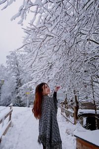 Woman standing by snow covered bare tree