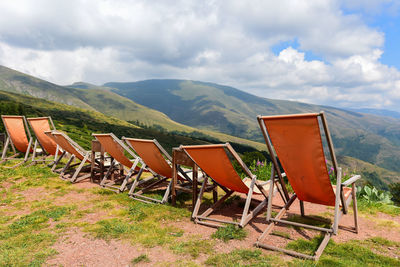 Deck chairs on field by mountains against sky