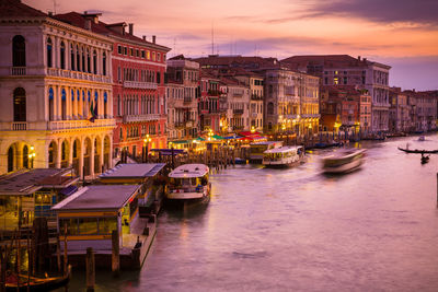 Boats moored in canal amidst buildings in city at sunset