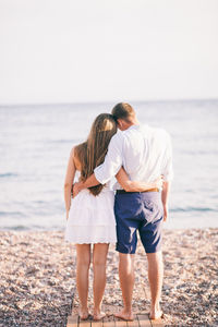 Rear view of couple standing on beach against clear sky