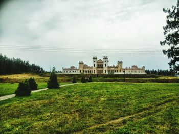 House on grassy field against cloudy sky