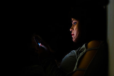 Side view of woman using mobile phone in dark