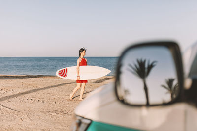 Woman with surfboard on beach against sky