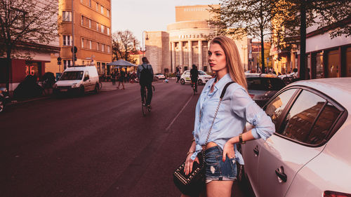 Beautiful young woman standing against car on street in city