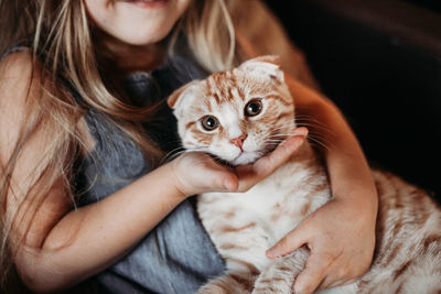 Midsection of girl holding cat while sitting at home