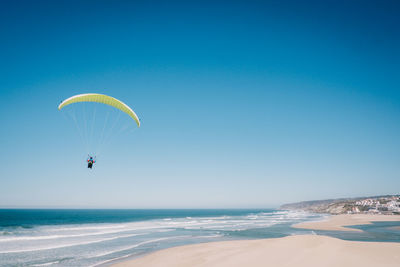 Person paragliding over sea against clear blue sky