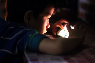 Close-up of boy using mobile phone at home in darkroom