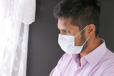 Close-up man wearing mask looking away standing by window