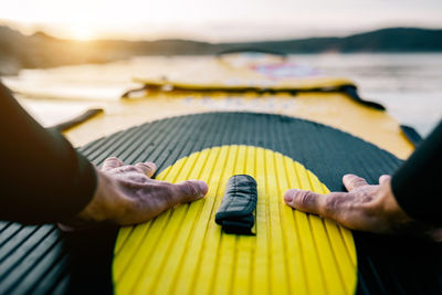 Pov view of crop hands of anonymous male surfer floating on sup board in sea at sunset