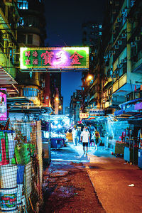 People walking on illuminated street against buildings at night