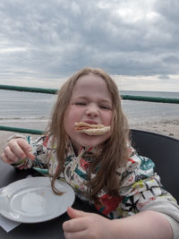Portrait of girl eating food against sky