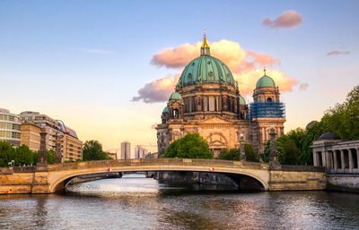 Bridge over river by buildings in city against sky