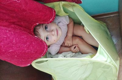 High angle view of girl wearing huge hat while sitting in laundry basket