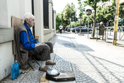 Senior man with weight scale sitting on sidewalk in city